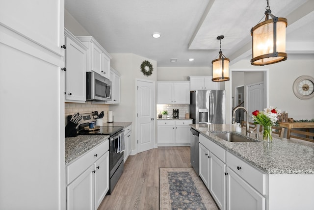 kitchen with white cabinets, an island with sink, appliances with stainless steel finishes, pendant lighting, and a sink