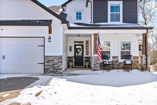 snow covered property entrance featuring an attached garage, stone siding, and a porch