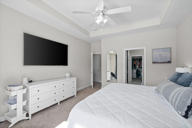 bedroom with light colored carpet, a ceiling fan, baseboards, a walk in closet, and a raised ceiling