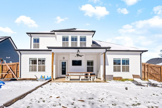 snow covered back of property with ceiling fan, fence, and a gate