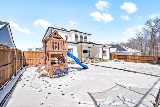 snow covered playground with a fenced backyard and a playground