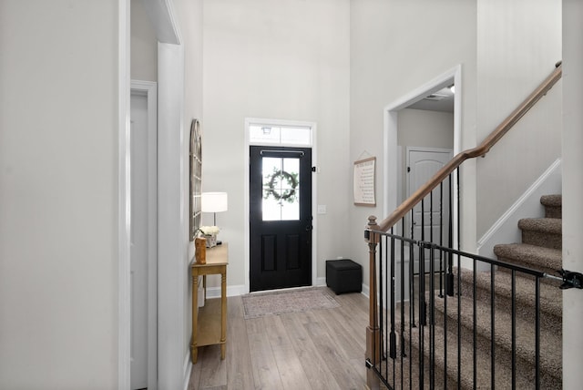 entryway with light wood-type flooring, stairs, a high ceiling, and baseboards