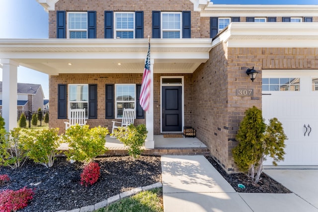 property entrance with a garage, covered porch, and brick siding