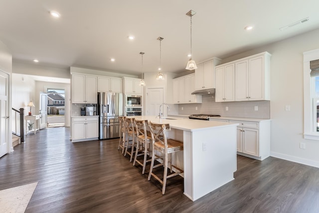 kitchen featuring under cabinet range hood, stainless steel appliances, visible vents, white cabinets, and decorative backsplash