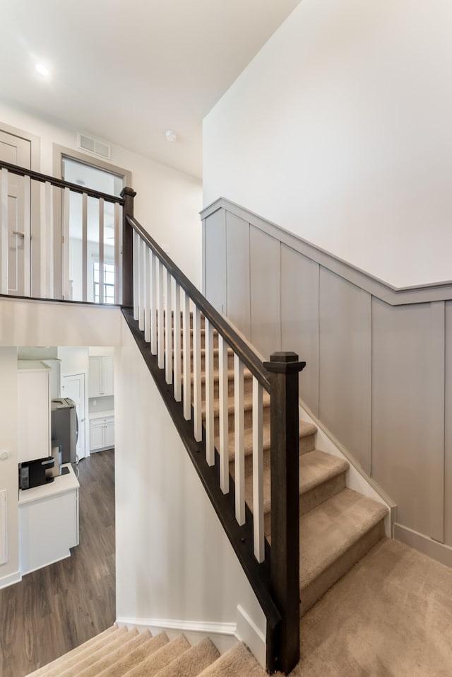 stairs with a wainscoted wall, visible vents, a decorative wall, and wood finished floors