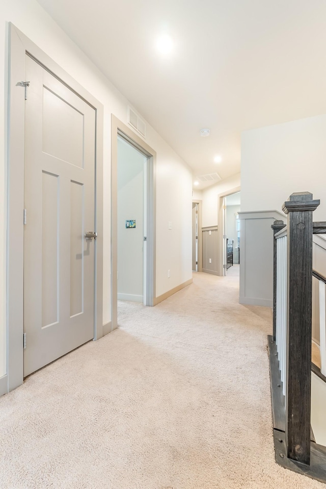 hall with light carpet, an upstairs landing, visible vents, and baseboards