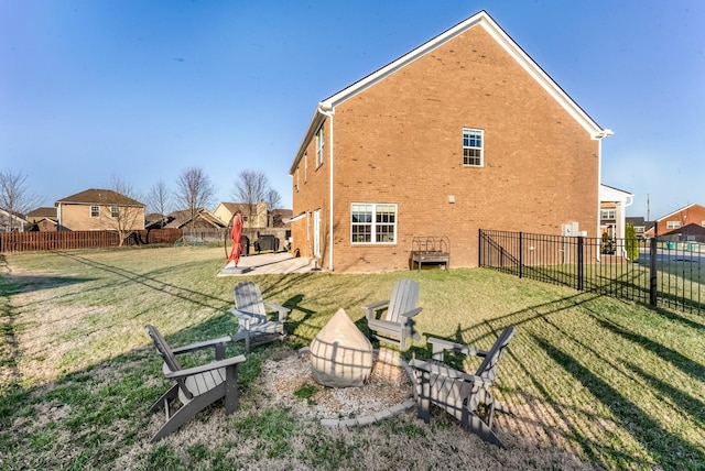 rear view of property featuring brick siding, a yard, a patio, an outdoor fire pit, and fence