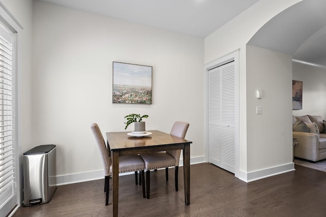 dining area featuring baseboards, dark wood finished floors, and arched walkways