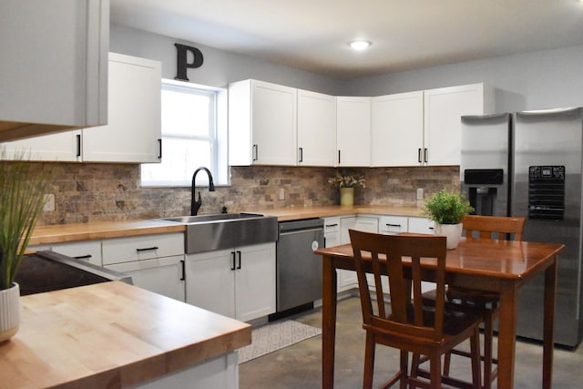 kitchen with concrete flooring, appliances with stainless steel finishes, butcher block countertops, and a sink