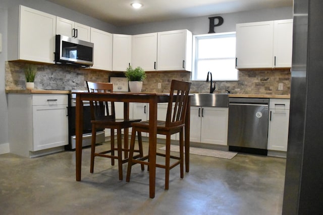 kitchen featuring a sink, white cabinetry, appliances with stainless steel finishes, decorative backsplash, and finished concrete floors