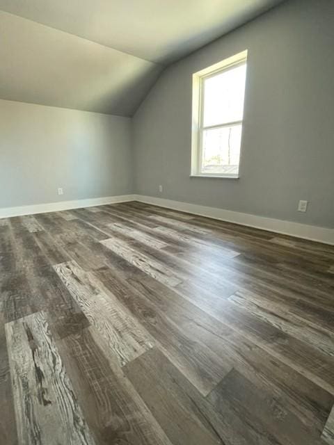 additional living space with dark wood-type flooring, lofted ceiling, and baseboards