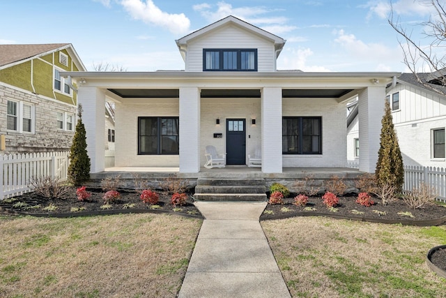 bungalow featuring covered porch, brick siding, a front lawn, and fence