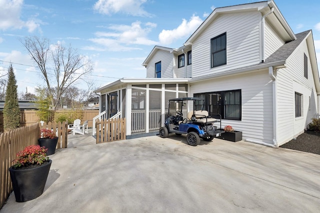 back of property with driveway, a sunroom, and fence