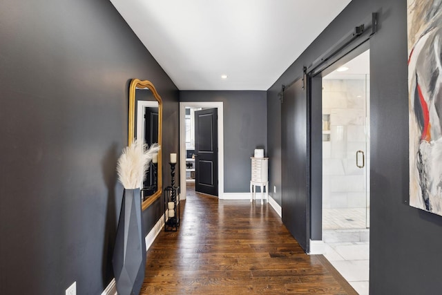 corridor featuring a barn door, baseboards, and dark wood-style flooring