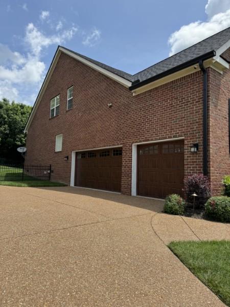 view of property exterior with brick siding, driveway, and fence