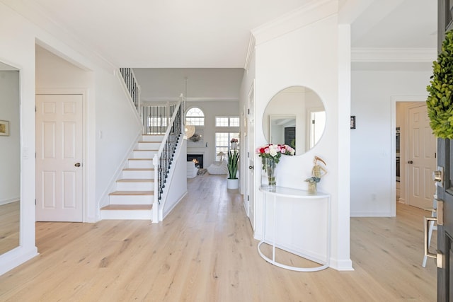 foyer entrance featuring baseboards, light wood-style floors, a lit fireplace, stairway, and crown molding