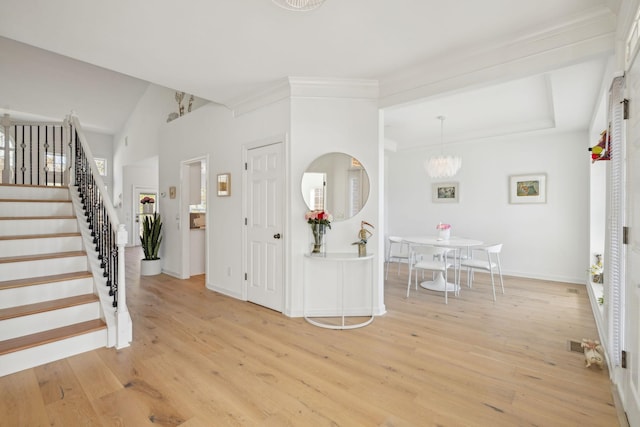 entrance foyer with baseboards, light wood-style flooring, ornamental molding, stairs, and a chandelier