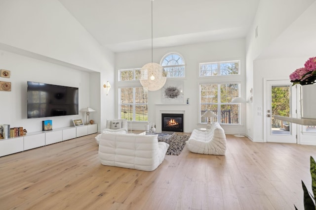 living room featuring a high ceiling, a glass covered fireplace, and light wood-style flooring