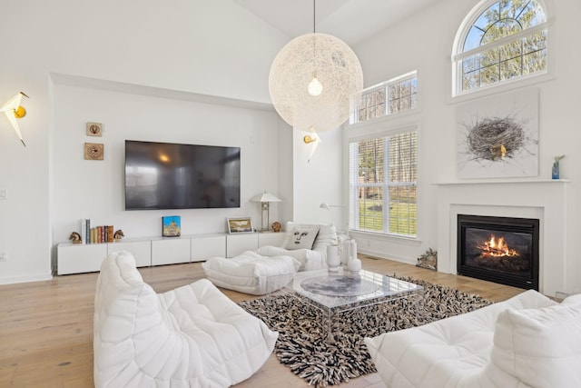 living room featuring high vaulted ceiling, light wood-type flooring, a glass covered fireplace, and baseboards