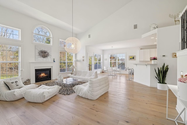 living area featuring high vaulted ceiling, a glass covered fireplace, light wood-style flooring, and baseboards