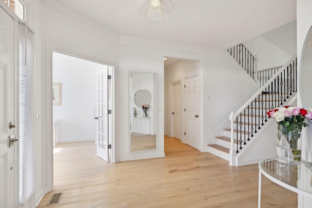 foyer featuring light wood-type flooring, stairs, visible vents, and ornamental molding