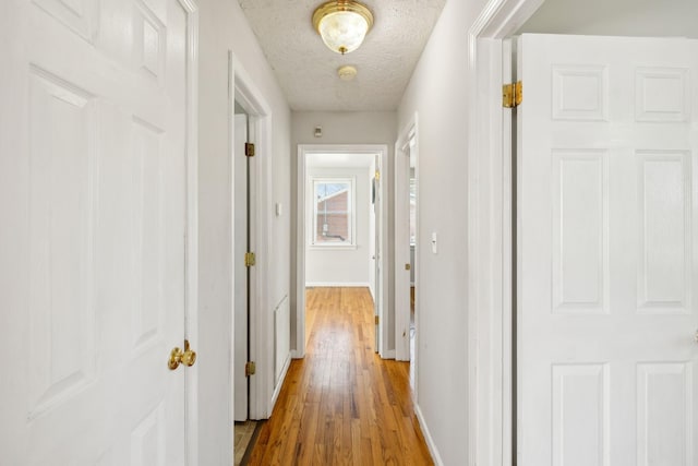 hallway with a textured ceiling, baseboards, and wood finished floors