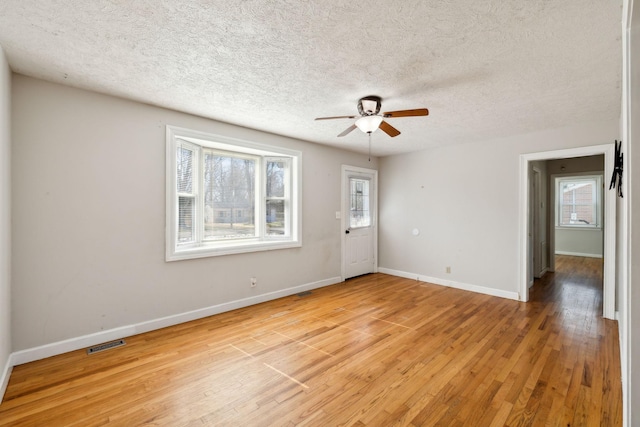 spare room featuring baseboards, visible vents, a ceiling fan, a textured ceiling, and light wood-style floors