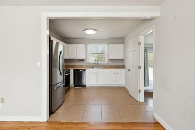 kitchen featuring light tile patterned floors, stainless steel appliances, white cabinetry, a sink, and baseboards