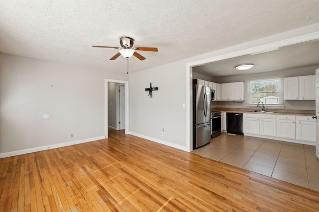 interior space with a sink, white cabinetry, light wood-style floors, black dishwasher, and freestanding refrigerator