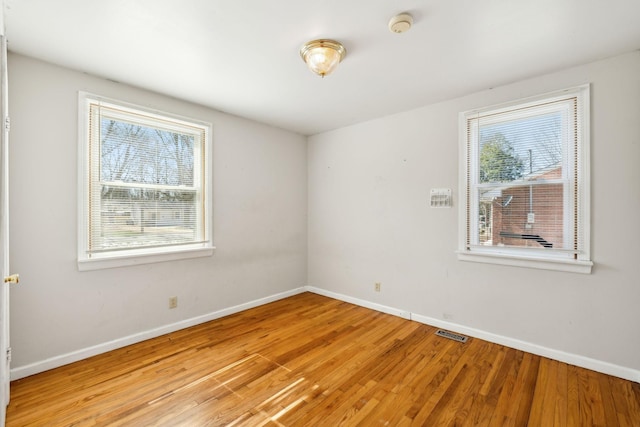 empty room featuring light wood-type flooring, visible vents, and baseboards