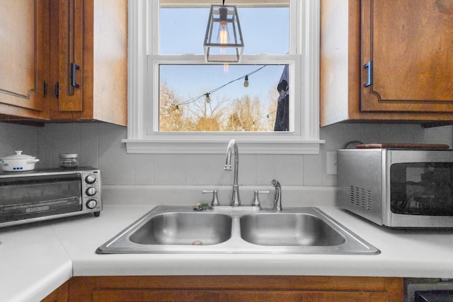 kitchen with a toaster, light countertops, stainless steel microwave, brown cabinetry, and a sink