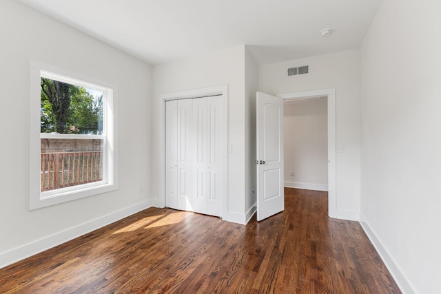 unfurnished bedroom featuring dark wood-style floors, a closet, visible vents, and baseboards