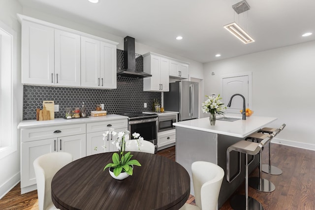 kitchen featuring a center island with sink, white cabinets, wall chimney exhaust hood, appliances with stainless steel finishes, and light countertops