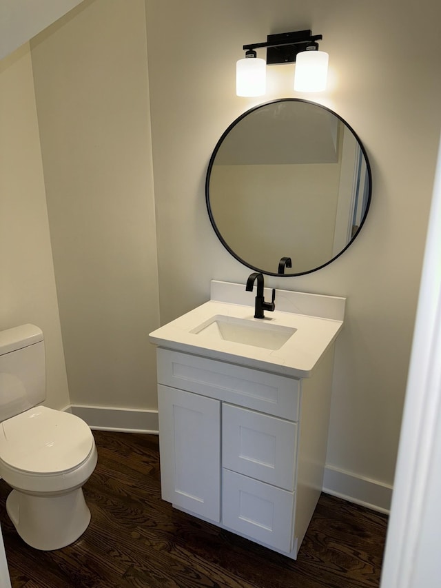 half bathroom featuring toilet, vanity, baseboards, and wood finished floors