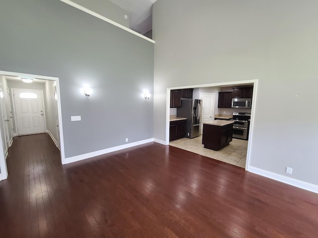 unfurnished living room with baseboards, a high ceiling, and light wood-style floors