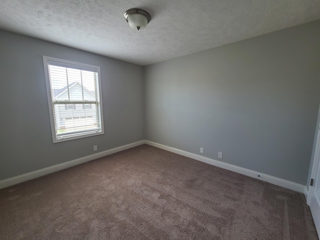 empty room featuring dark colored carpet, a textured ceiling, and baseboards