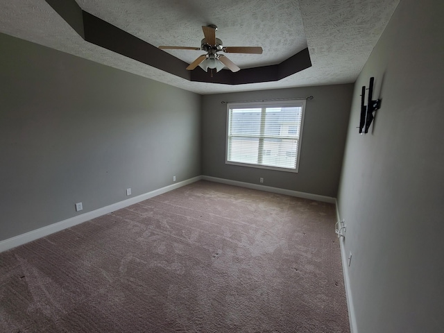 unfurnished room with a tray ceiling, a ceiling fan, light carpet, a textured ceiling, and baseboards