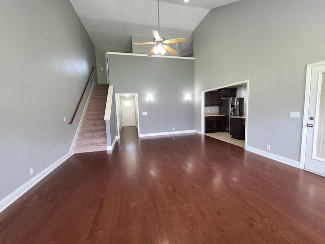 unfurnished living room with dark wood-type flooring, ceiling fan, baseboards, and stairs