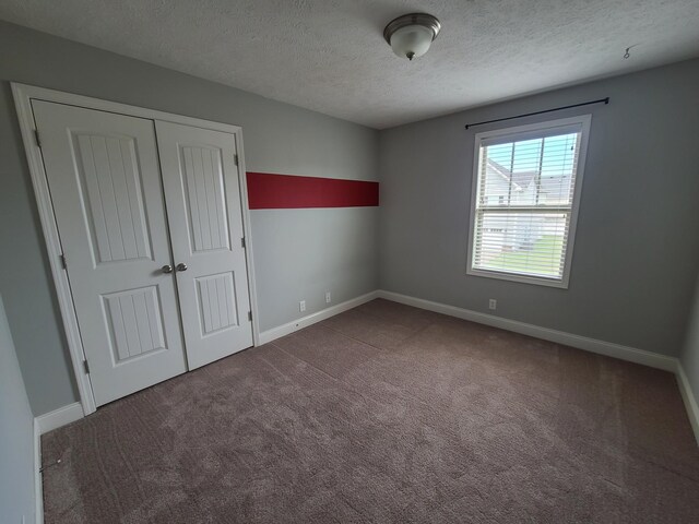 unfurnished bedroom with carpet, a closet, a textured ceiling, and baseboards