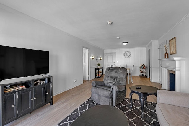 living area with light wood-style flooring, a fireplace, ornamental molding, and baseboards