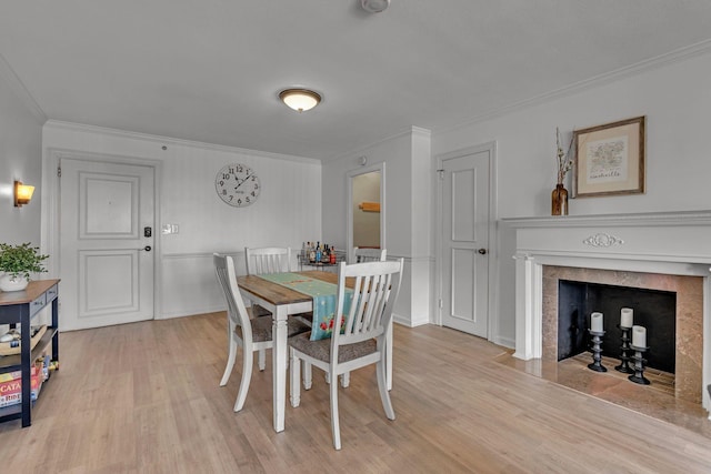 dining room with light wood-style flooring, ornamental molding, baseboards, and a fireplace with flush hearth