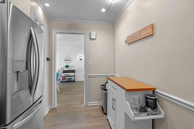 interior space with stainless steel refrigerator with ice dispenser, light wood finished floors, butcher block counters, ornamental molding, and white cabinetry