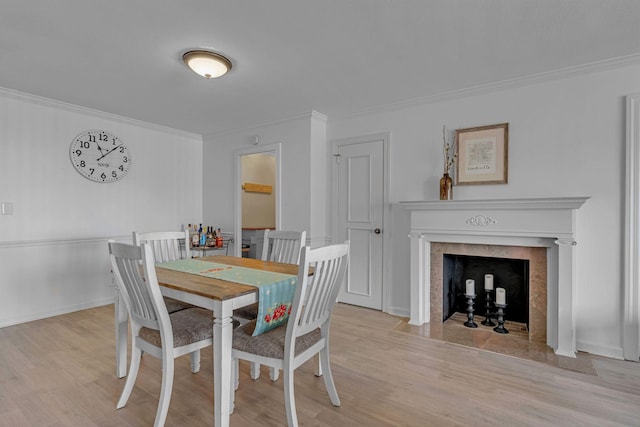 dining area with light wood-style floors, a high end fireplace, crown molding, and baseboards