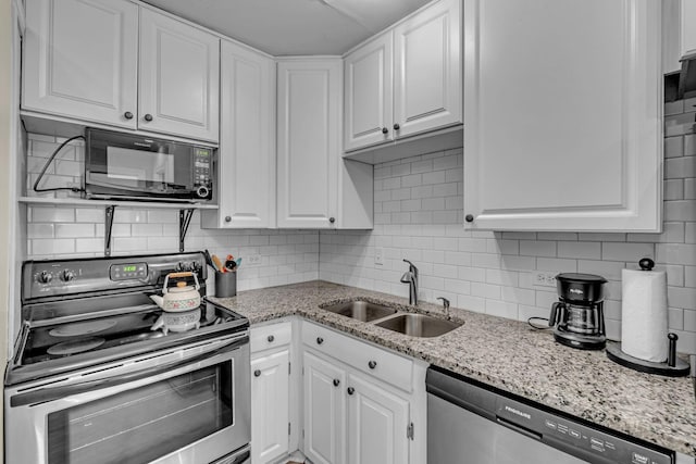 kitchen featuring light stone counters, stainless steel appliances, decorative backsplash, white cabinetry, and a sink