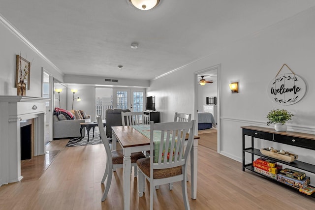 dining area with french doors, crown molding, visible vents, light wood-style floors, and a fireplace with flush hearth