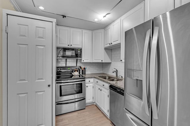 kitchen with light wood-style flooring, appliances with stainless steel finishes, white cabinetry, a sink, and light stone countertops