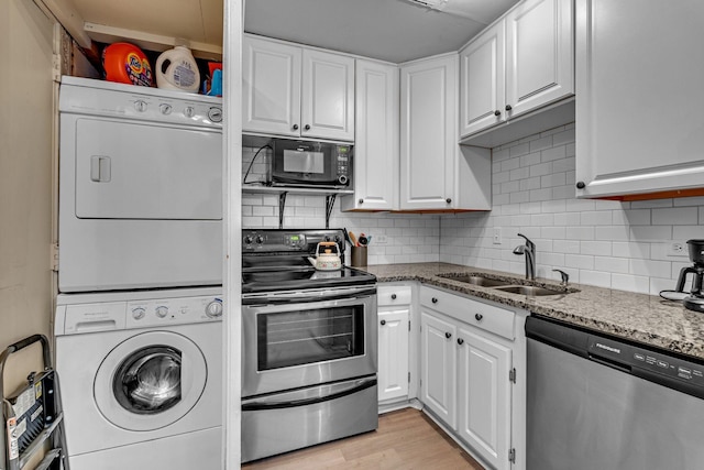 kitchen with light stone counters, stainless steel appliances, a sink, white cabinets, and stacked washing maching and dryer