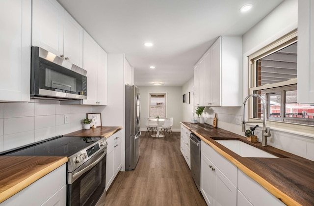 kitchen with dark wood finished floors, stainless steel appliances, white cabinetry, a sink, and wood counters