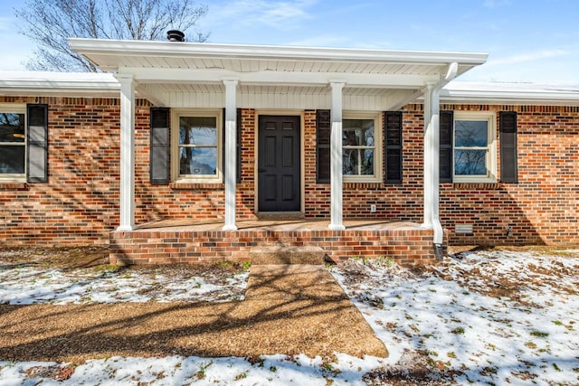 snow covered property entrance with covered porch and brick siding