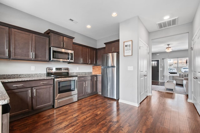 kitchen with appliances with stainless steel finishes, dark brown cabinetry, visible vents, and light stone countertops